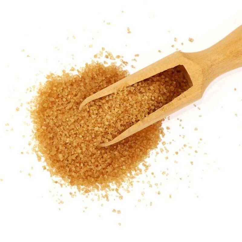 SUGAR4 Close up one wooden scoop spoon full of raw brown cane sugar with pinch spilled and spread around, isolated on white background, elevated top view, directly above